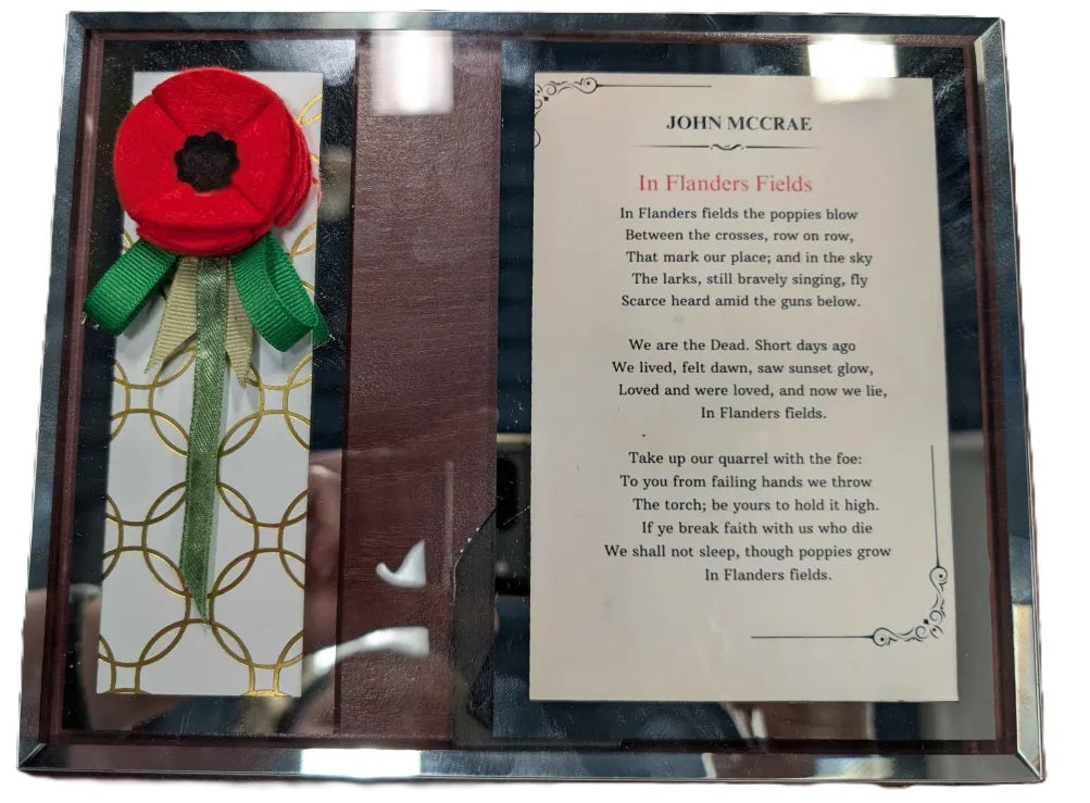 Decorative item with a red poppy, green ribbon, and poem card on a glass frame.
