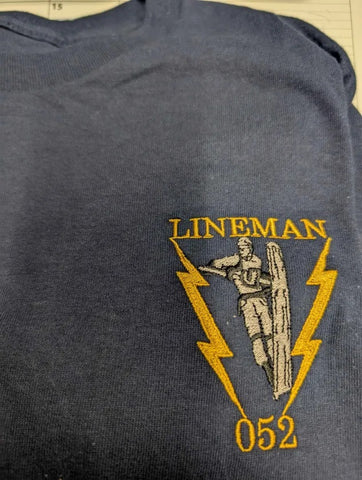 Dark blue shirt with 'LINEMAN 052' embroidered design featuring a lineman and lightning bolts.
