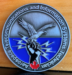 Front image of the coin has "Aerospace Telecommunications and Information System Technicial" along the outside and an image with a bird sitting on a fish clenching lightning bolts. There is also a red maple leaf at the bottom. The area that has the fist is blue.