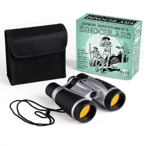 A pair ob binoculars sits in front of a black case and a green box. On the box is a man looking through binoculars and the words "Junior Adventure's Binoculars"