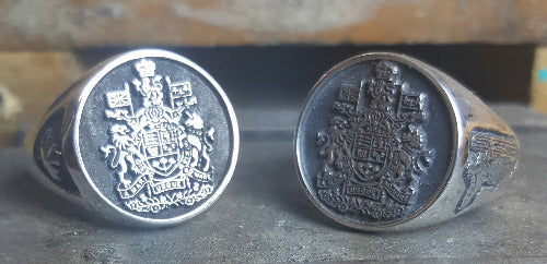 Two silver rings are shown, both have the Chief Warrant Officer Crest. The one on the left has a maple leaf on the shoulder and the one on the right has the lineman on a pole on the shoulder.