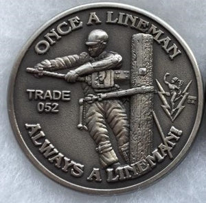 "Once a Lineman Always a Lineman" coin with "trade 052" and lineman on a pole graphic, in the one corner is the mercury with bolts.