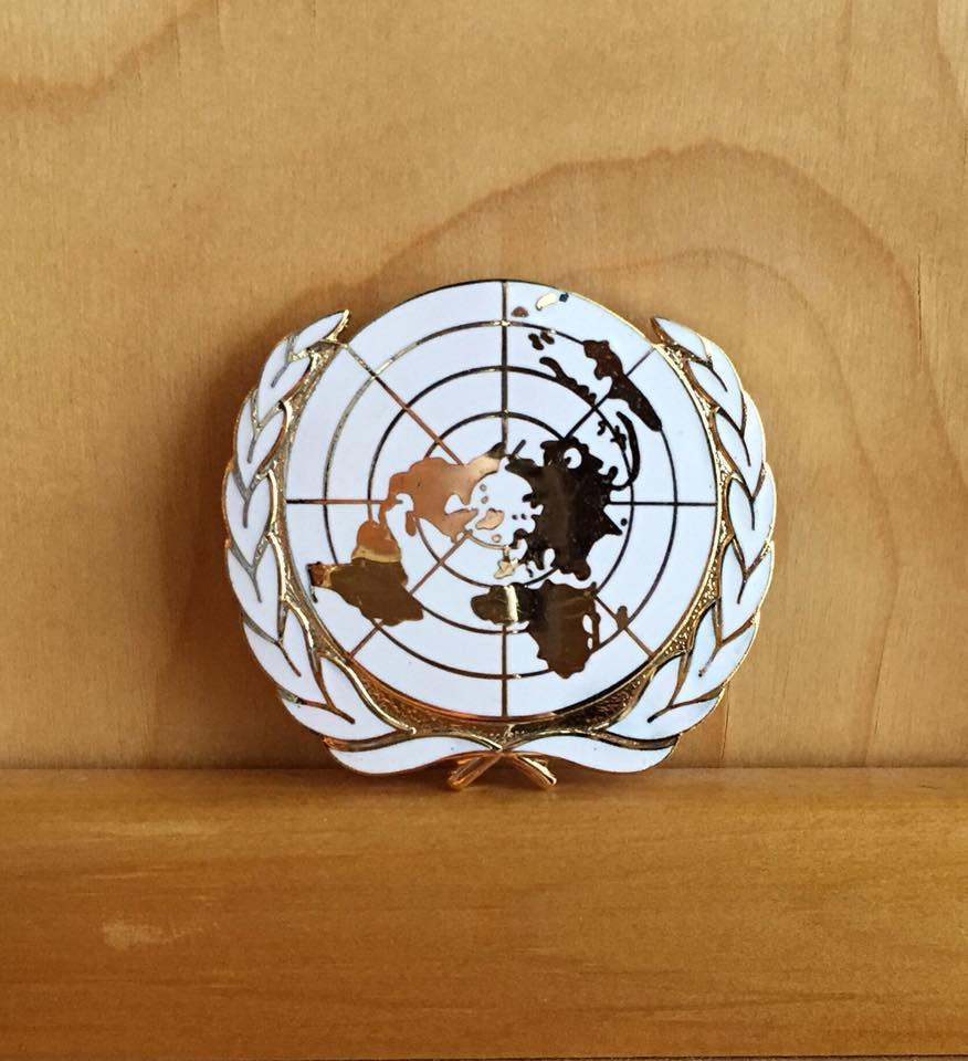White and gold metal UN cap badge.